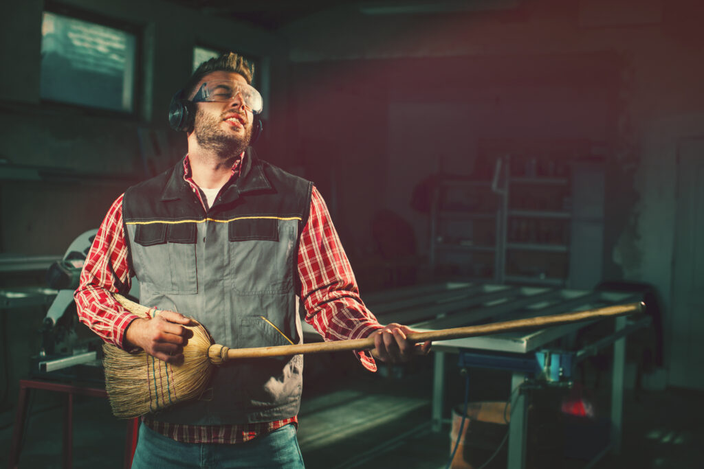 Young man on break at work has a headphones and holds a broom in his hands and pretending to play the guitar